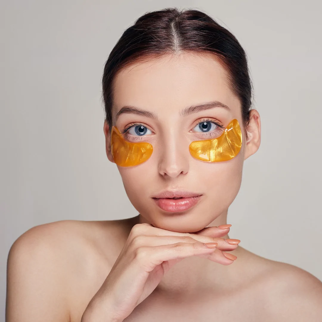 Mujer joven con parches dorados en la zona de las ojeras para el tratamiento del contorno de ojos. Cuidado estético y revitalización en Clínica Alcolea