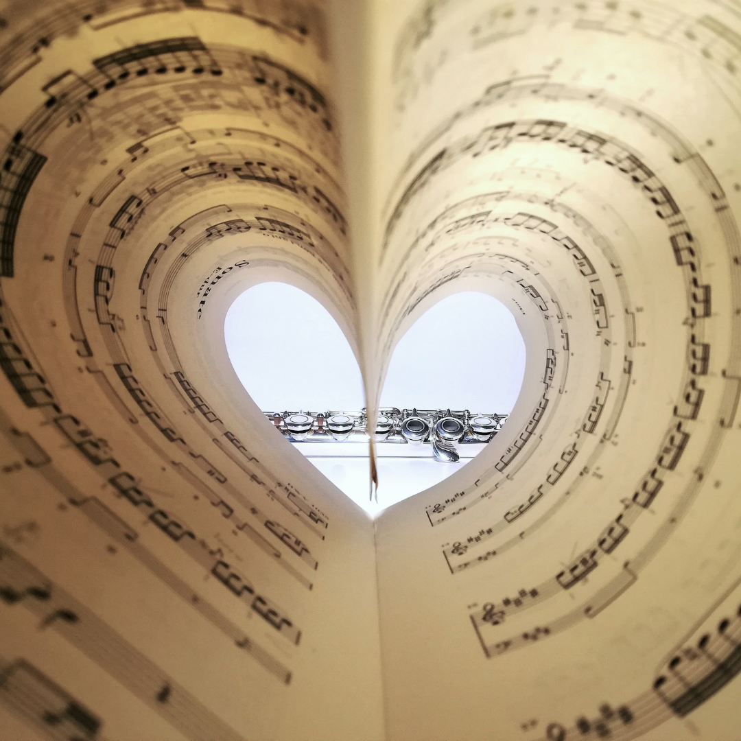 Partitura doblada con forma de corazón junto a una flauta, símbolo de la relación entre la música, las emociones y el bienestar cardiovascular.